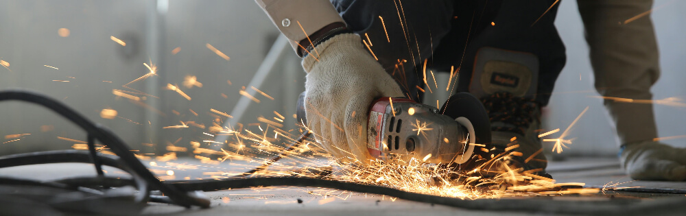 Gewerbliche Sachversicherung Eine Person arbeitet mit einem Winkelschleifer und erzeugt Funken. Sie trägt Arbeitshandschuhe und bearbeitet eine Metalloberfläche, während Funken sprühen.